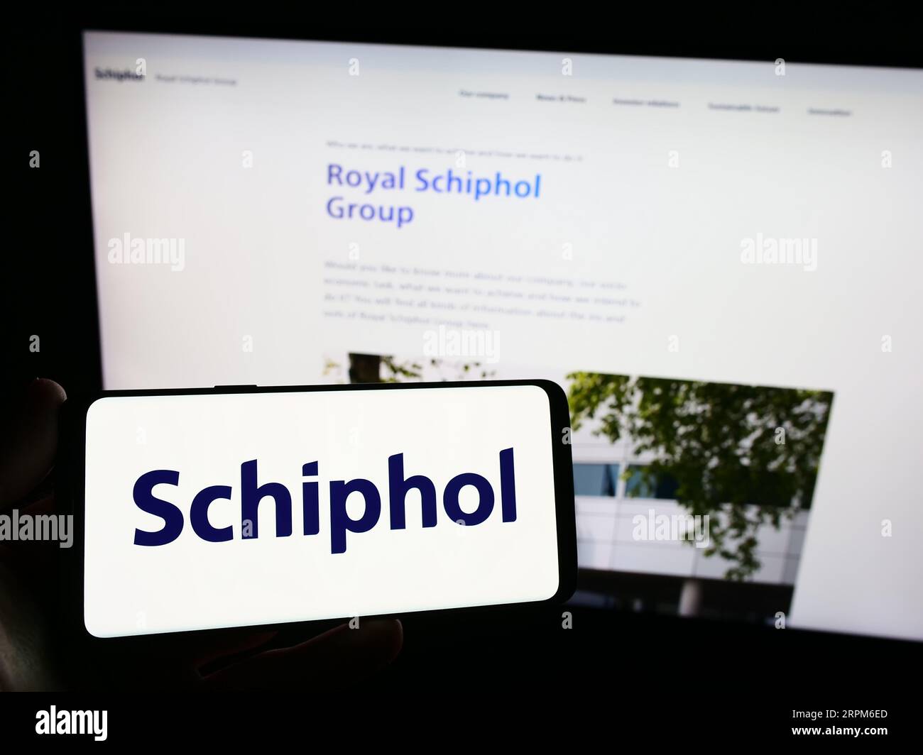 Person holding smartphone with logo of Dutch airport company Royal Schiphol Group N.V. on screen in front of website. Focus on phone display. Stock Photo