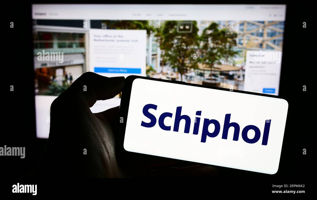 Person holding cellphone with logo of Dutch airport company Royal Schiphol Group N.V. on screen in front of webpage. Focus on phone display. Stock Photo