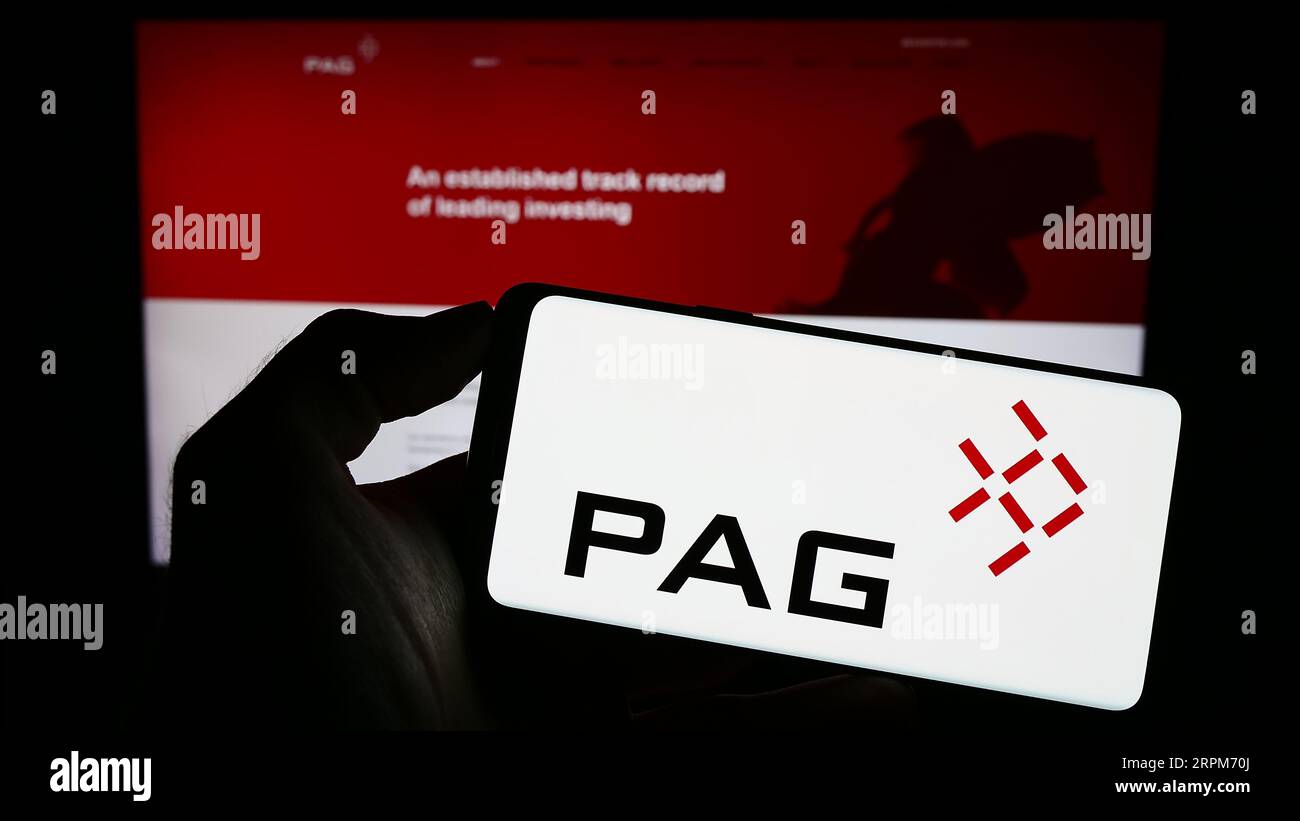 Person holding mobile phone with logo of Asian investment company PAG on screen in front of business web page. Focus on phone display. Stock Photo