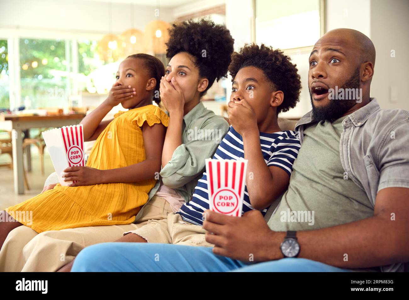 Frightened Family Eating Popcorn At Home Sitting On Sofa Streaming Horror Show Or Movie To TV Stock Photo