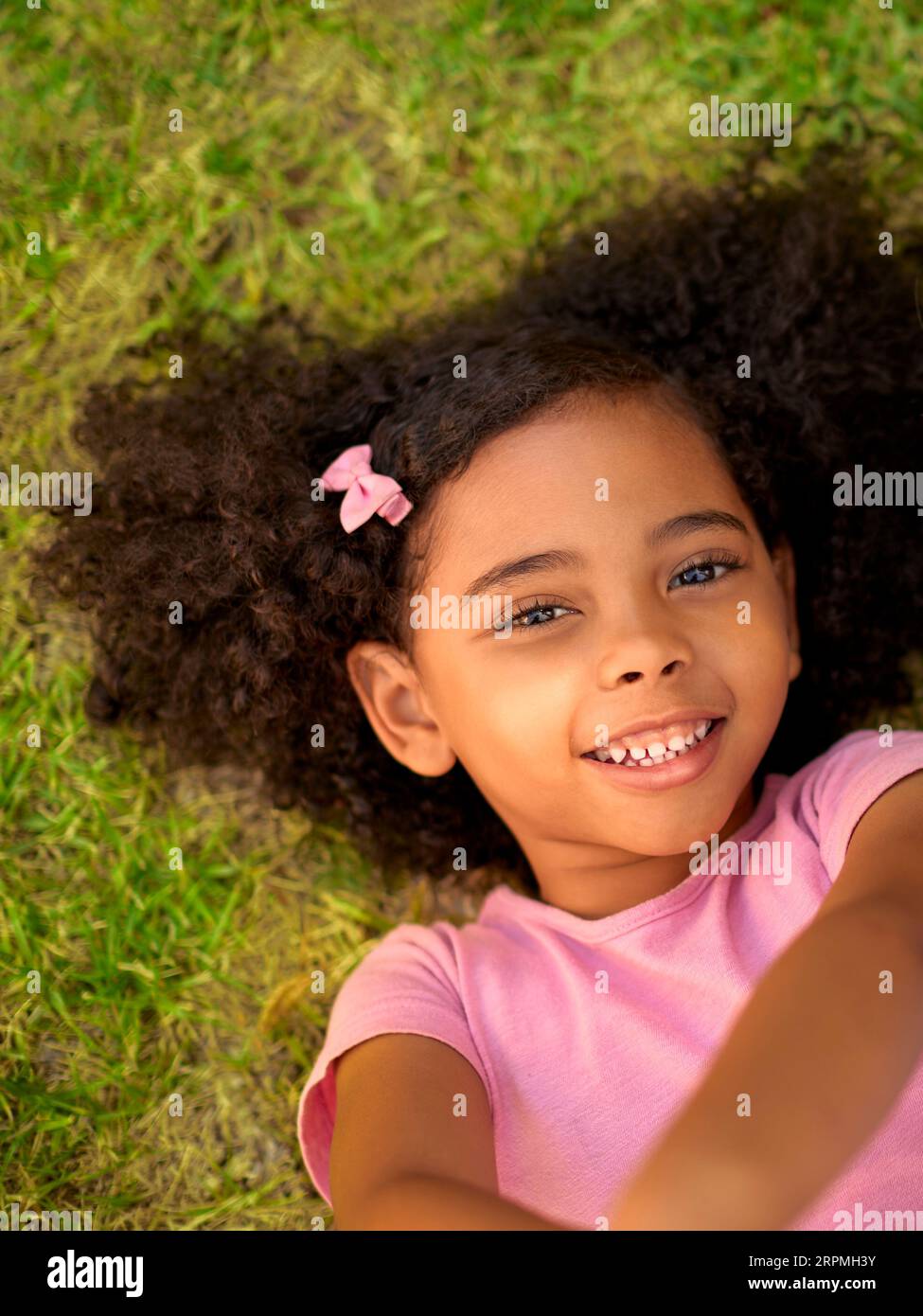 POV Overhead Shot Of Smiling Girl Lying On Grass Taking Selfie On Mobile Phone Stock Photo