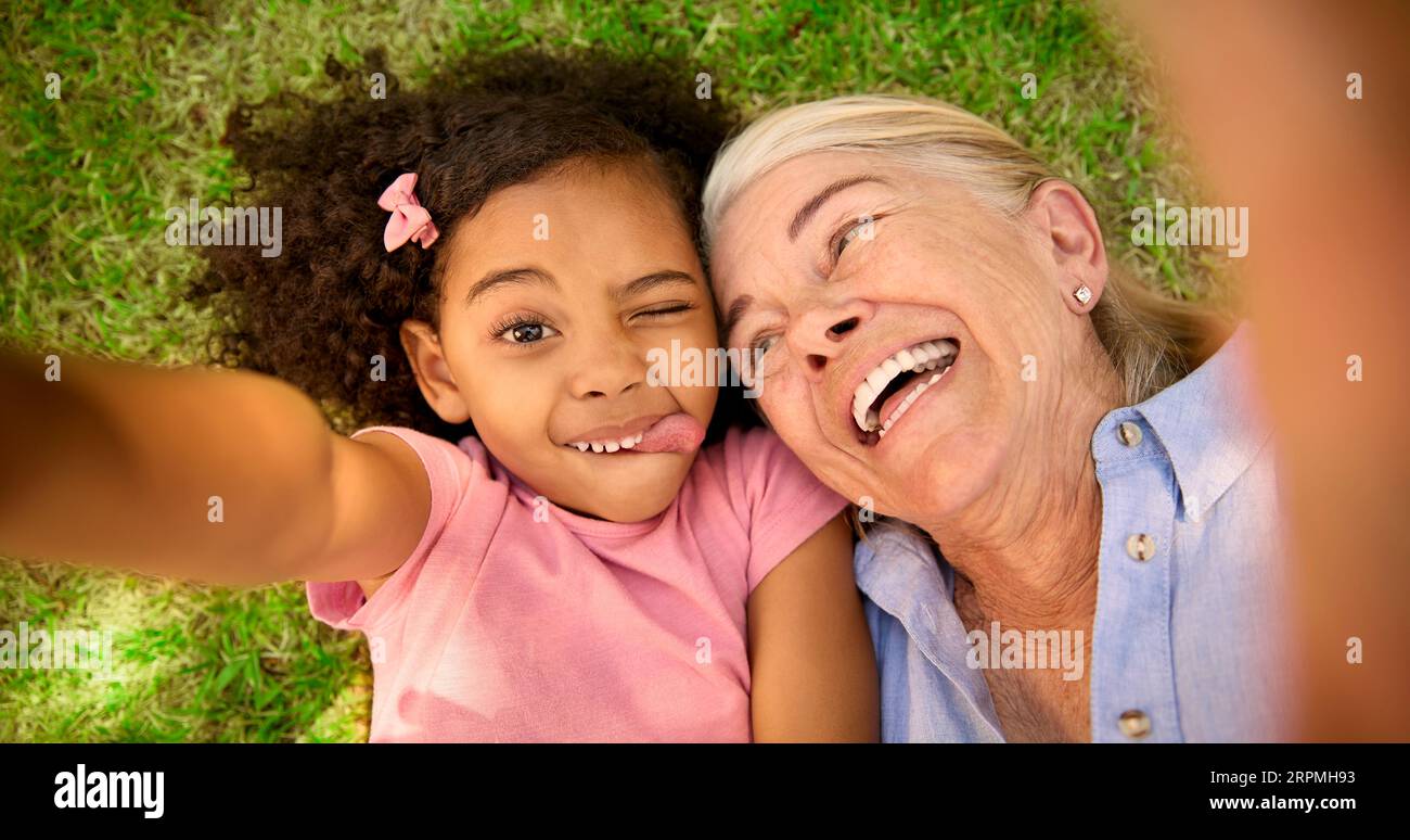 POV Overhead Shot Of Grandmother And Granddaughter Lying On Grass Taking Selfie On Mobile Phone Stock Photo