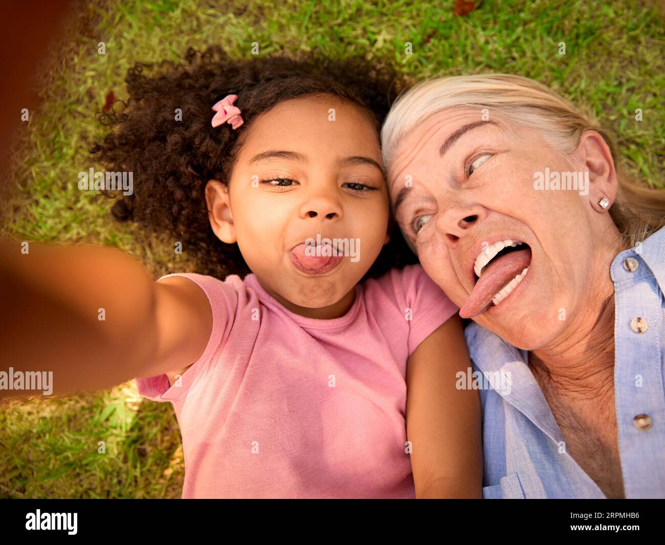 POV Overhead Shot Of Grandmother And Granddaughter Lying On Grass Taking Selfie On Mobile Phone Stock Photo