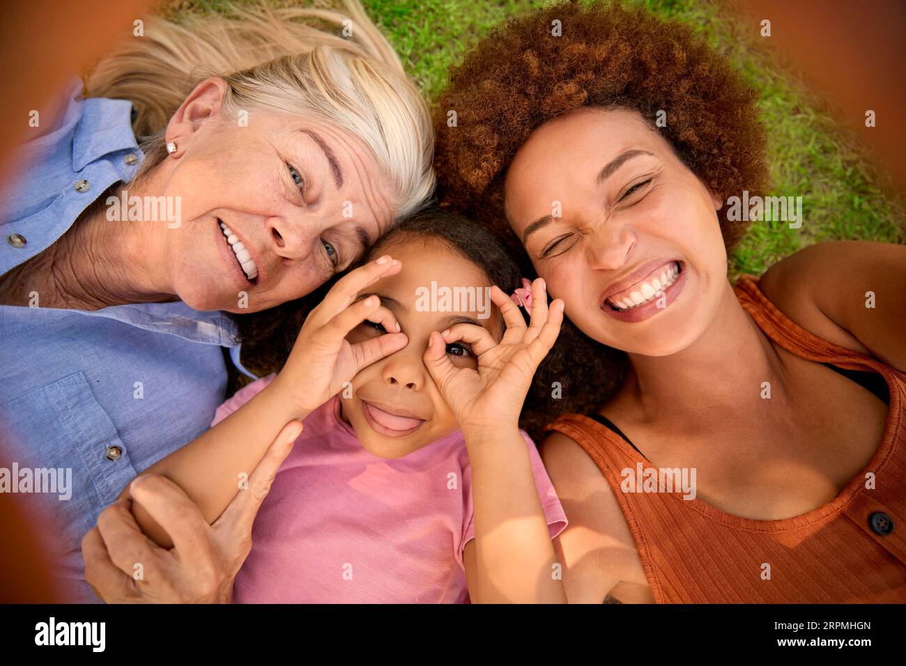 POV Overhead Shot Of Multi-Generation Female Family Lying On Grass Taking Selfie On Mobile Phone Stock Photo