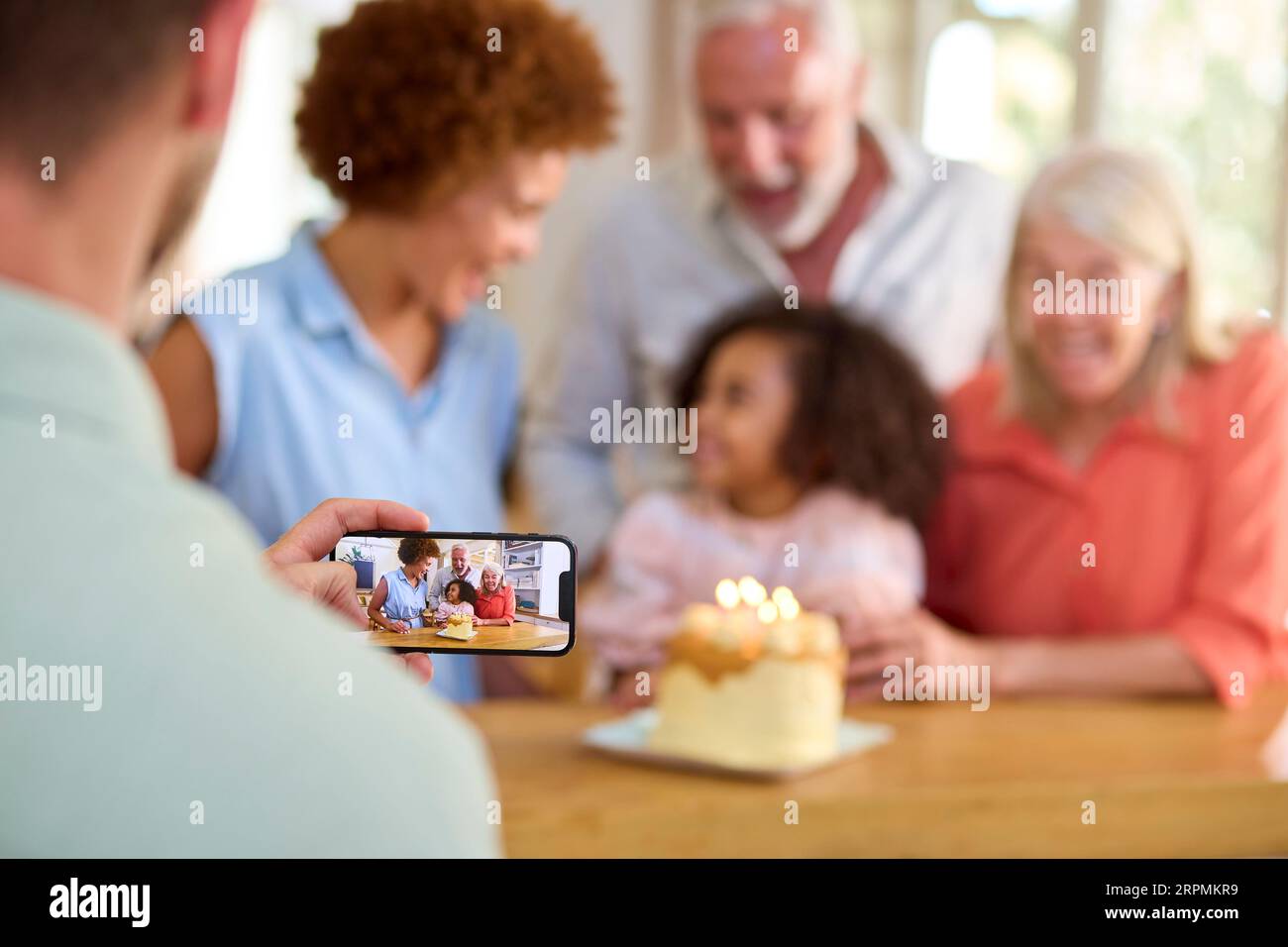 Dad Takes Photo As Multi-Generation Family Celebrate Granddaughter's Birthday At Home With Cake Stock Photo