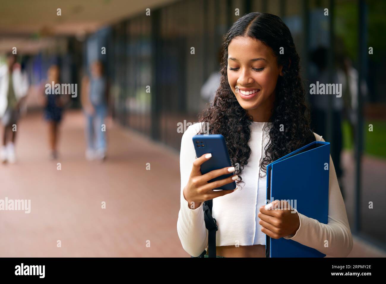 Female Secondary Or High School Student Outdoors At School Going To Class Looking At Mobile Phone Stock Photo