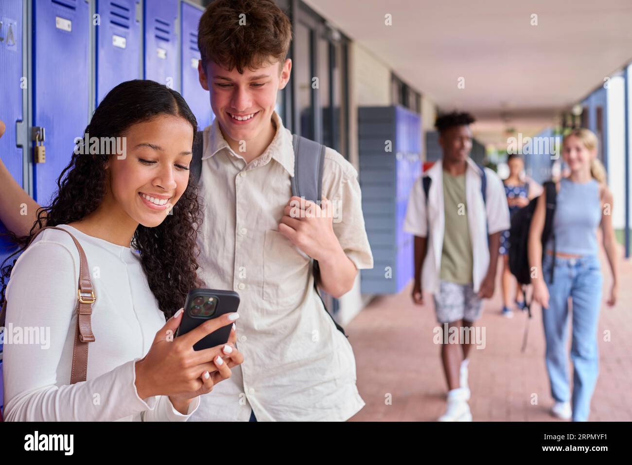 Male And Female Secondary Or High School Students Outdoors At School Looking At Mobile Phone Stock Photo