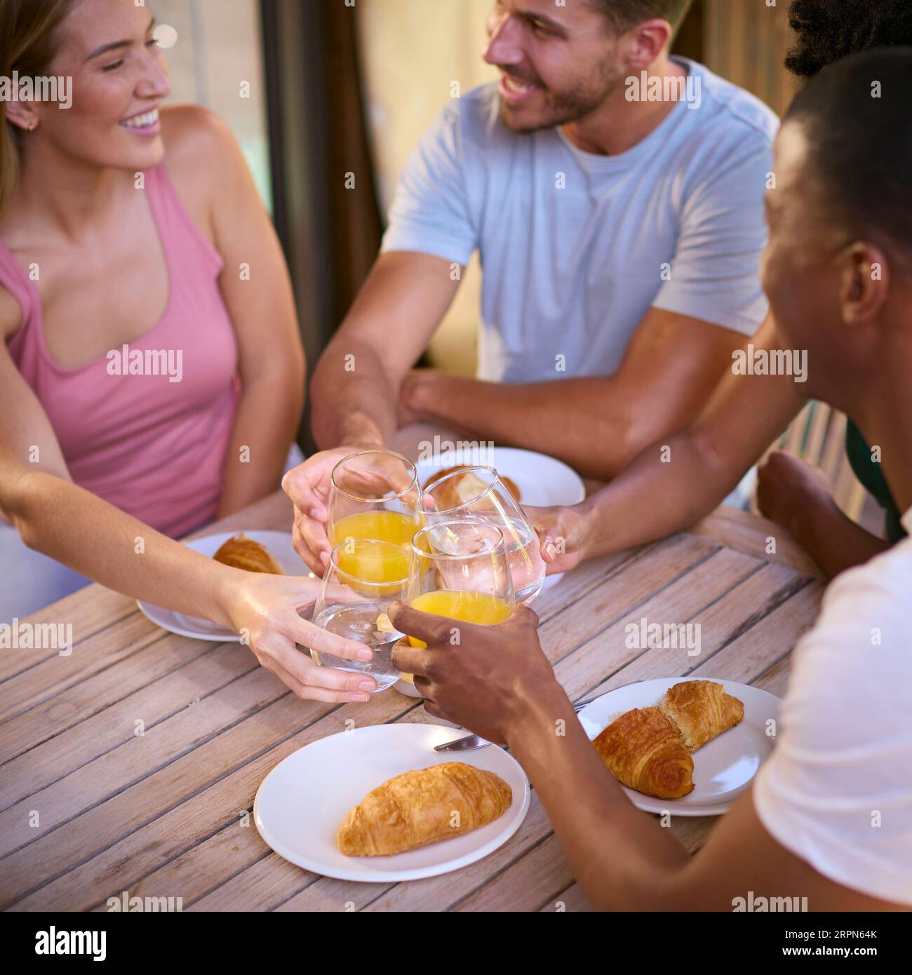 Group Of Smiling Multi-Cultural Friends Eating Breakfast Outdoors At Home Making A Toast Together Stock Photo