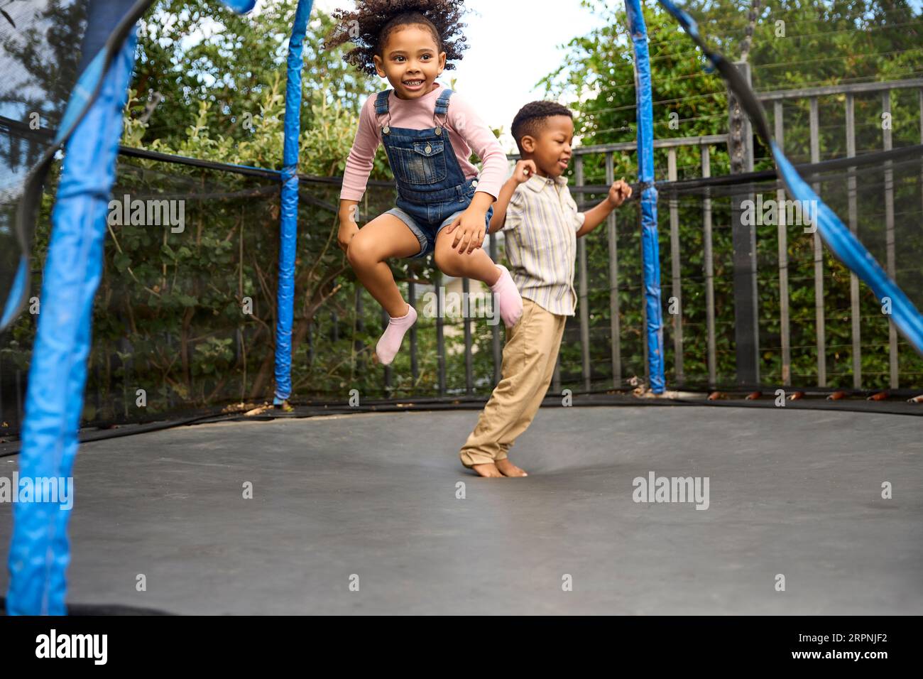 Boy And Girl Having Fun Playing In Garden Bouncing On Trampoline Stock