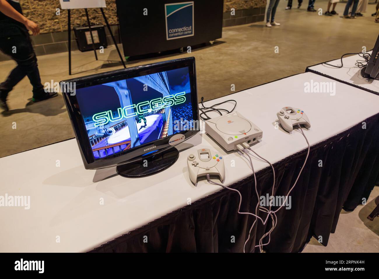 A Sega Dreamcast with two controllers available for free play at the Retro World Expo sitting on a white table with Success on the screen Stock Photo