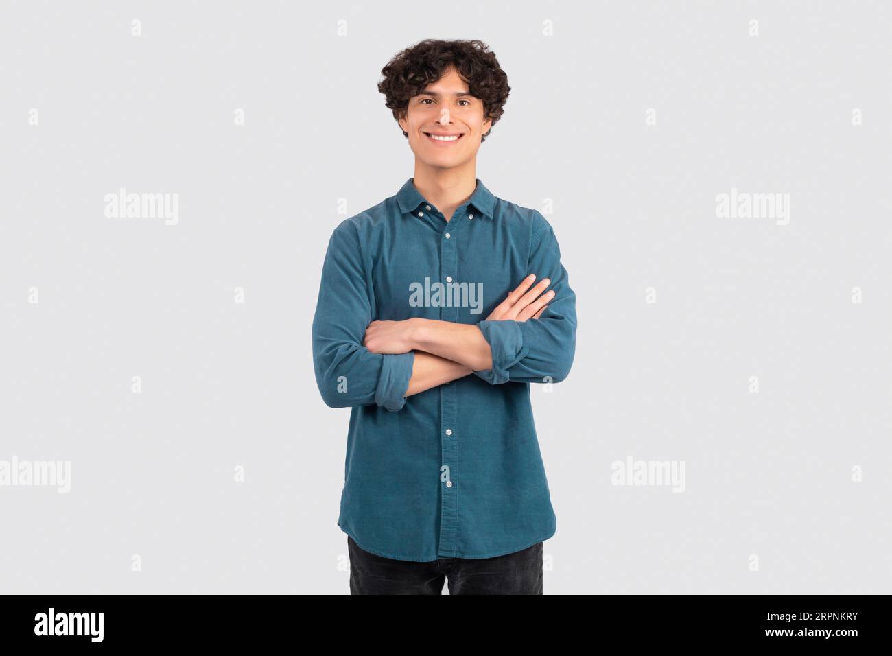 Positive Curly Young Man Posing Crossing Hands Over White Background Stock Photo