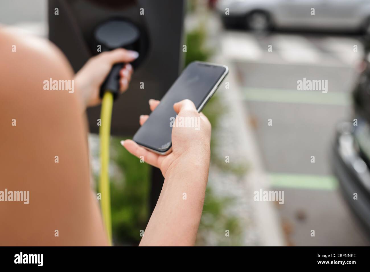 Girl connecting her electric car and a charging station with a cable ...