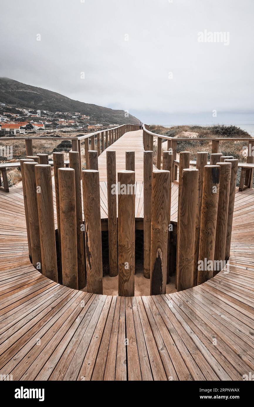 Boardwalk with wooden roundabout in Quiaios Beach connecting to the village and mountain in the background Stock Photo