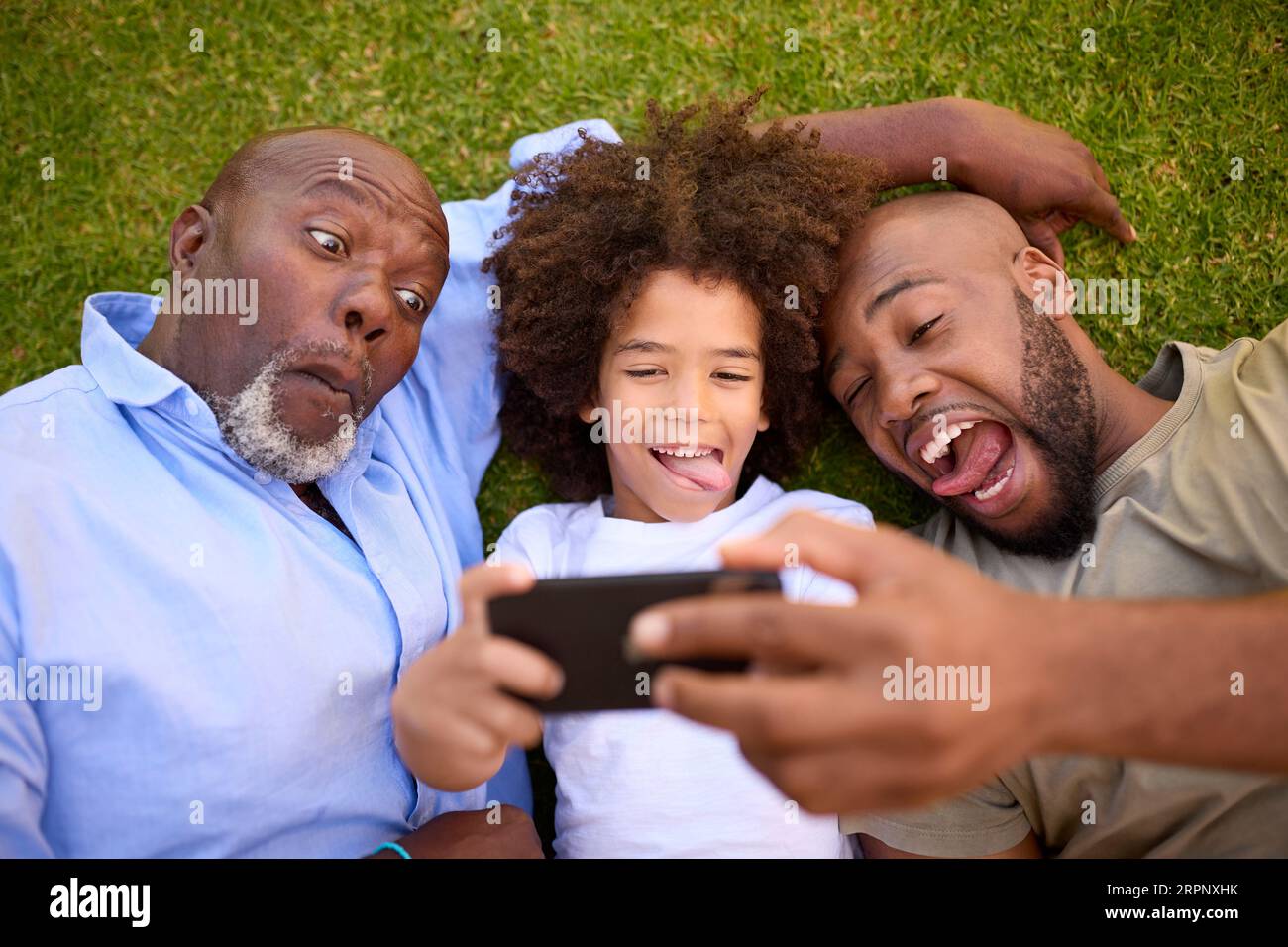 Overhead Shot Of Multi-Generation Male Family Lying On Grass Taking Selfie On Mobile Phone Stock Photo
