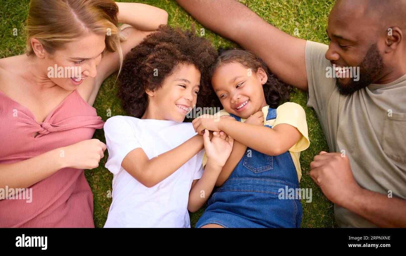 Overhead Shot Of Multi-Racial Family Lying On Grass Tickling Children Stock Photo