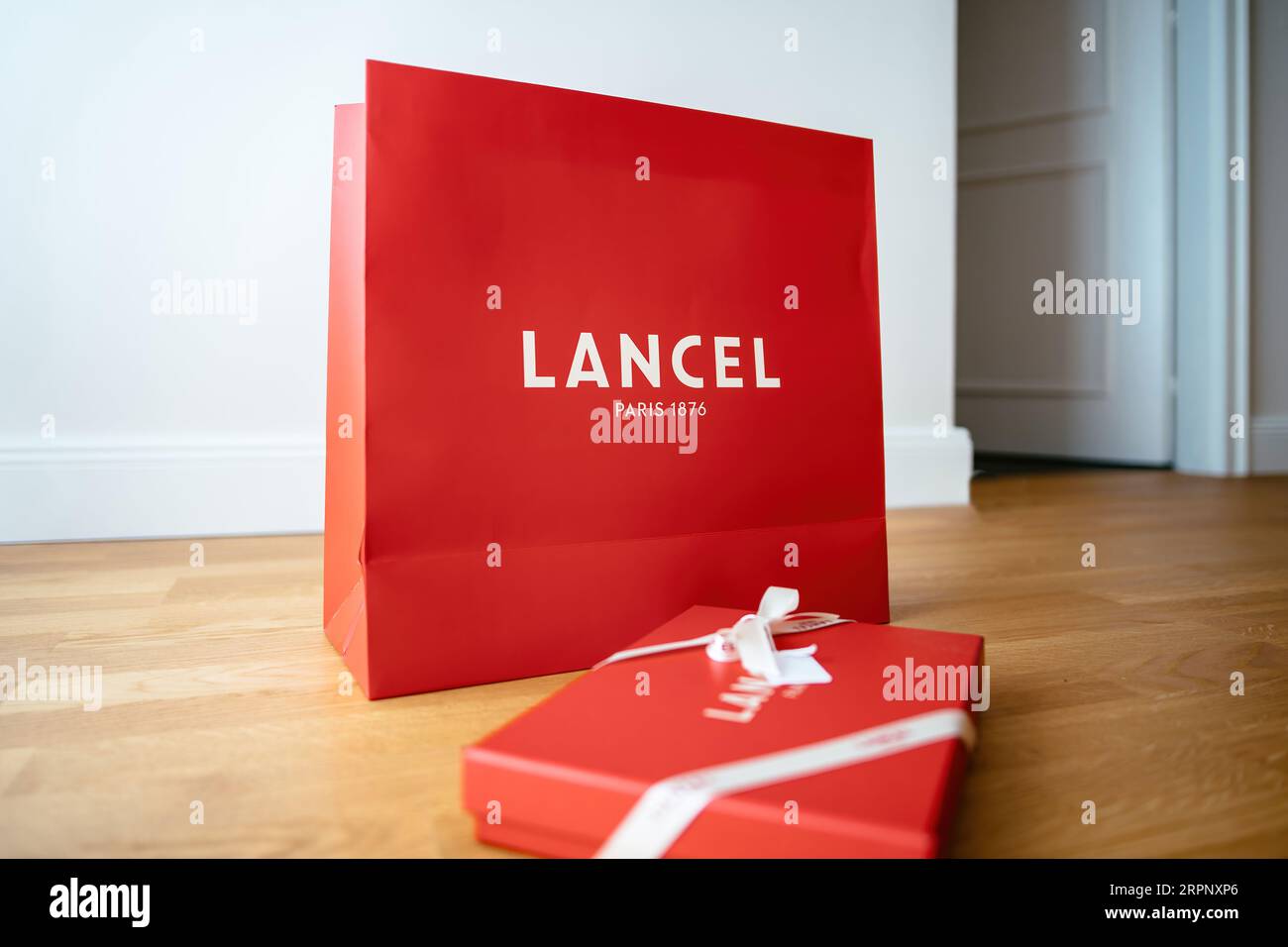 Paris, France - Aug 25, 2023: Side view of Lancel Paris branded red gift box with elegant logotype and silk ribbon on he wooden floor. A symbol of luxury and sophistication. Perfect for presentations and events. Stock Photo