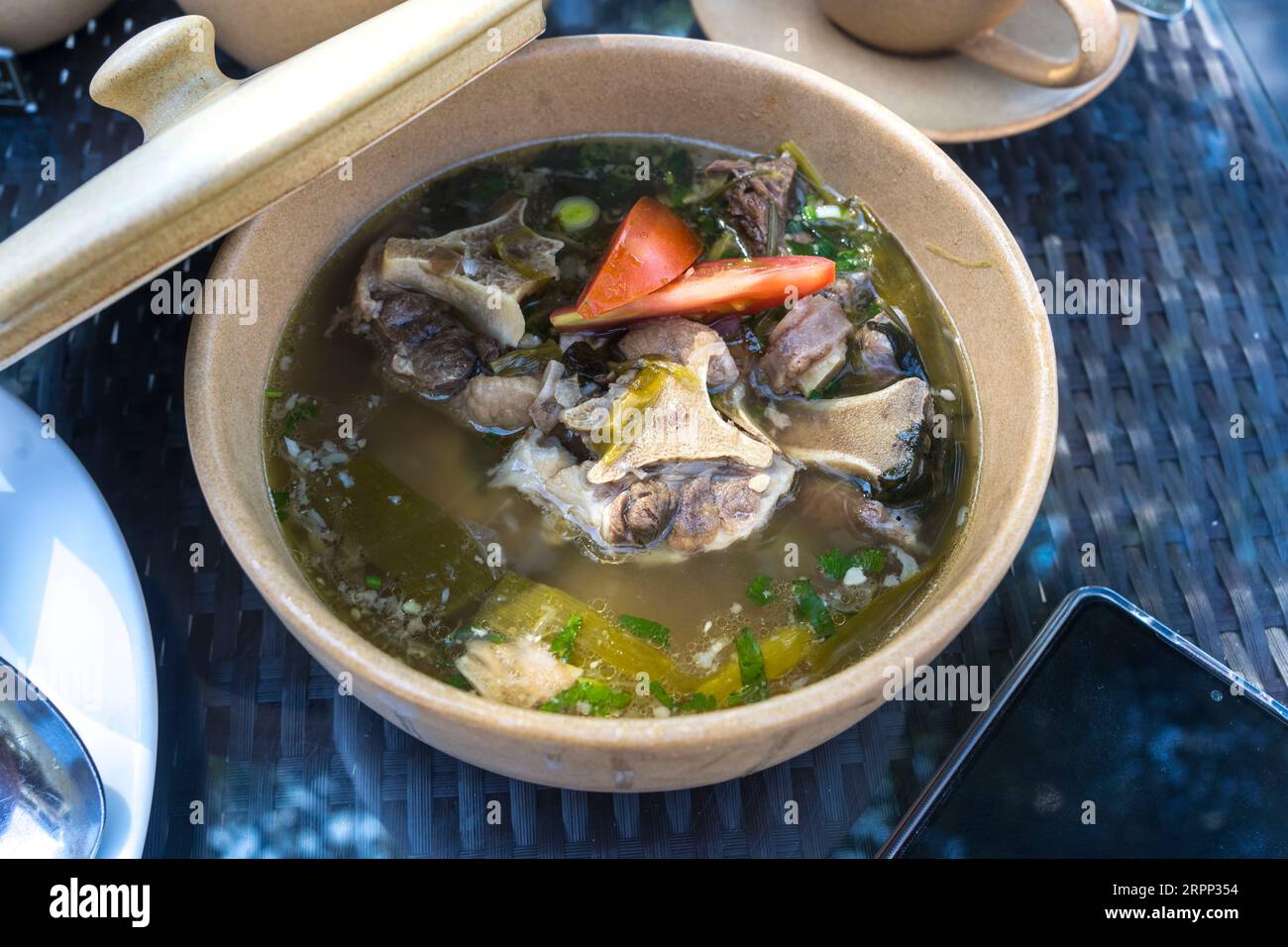 Traditional Indonesian Oxtail Soup served in a ceramic bowl with an open lid. Rich and flavorful featuring tender oxtail meat served in a savory broth Stock Photo