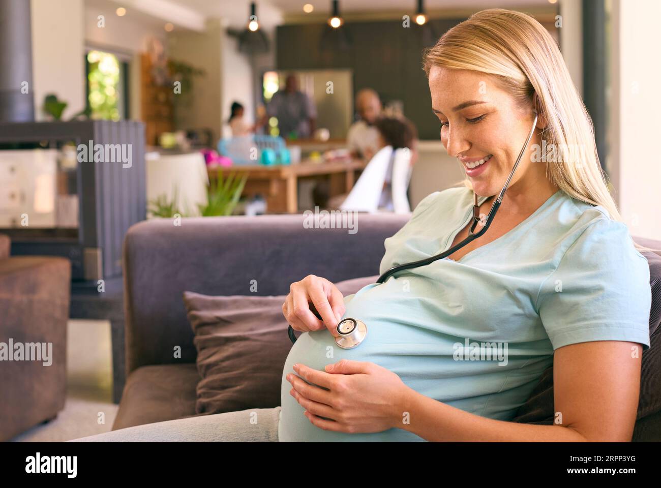 Pregnant Woman At Home Listening To Baby Heartbeat With Stethoscope Stock Photo