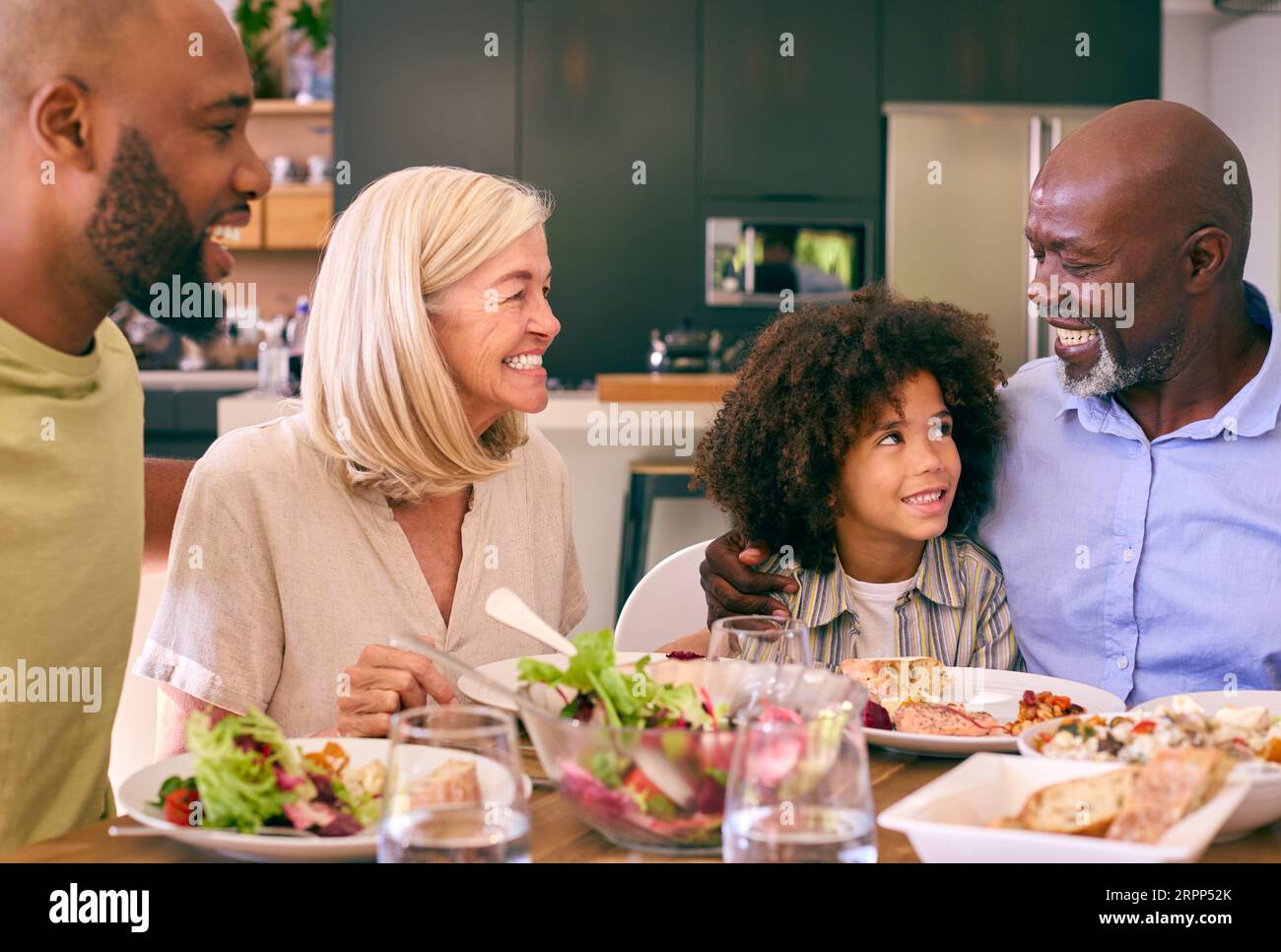 Multi-Generation Family Sitting Around Table Serving Food For Meal At Home Stock Photo