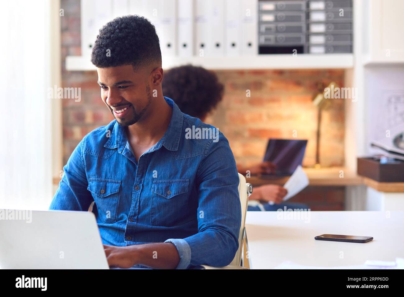 Young Smiling Businessman Working On Laptop At Desk In Office Stock Photo