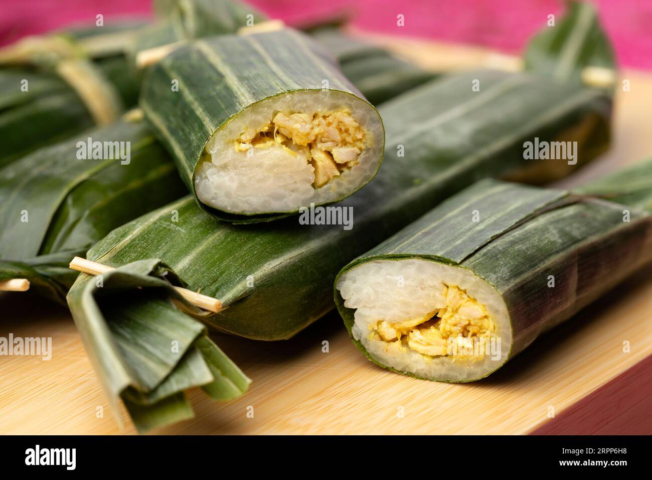 Whole and halved Lemper Ayam wrapped in banana leaves, an Indonesian savoury snack made of glutinous rice filled with seasoned shredded chicken close Stock Photo
