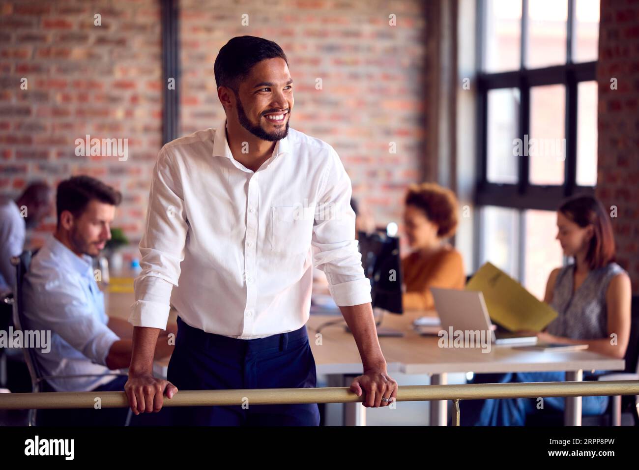 Portrait Of Smiling Businessman Standing In Busy Office Stock Photo