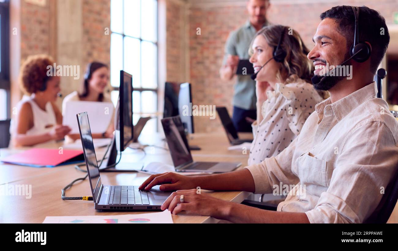 Multi-Cultural Business Team Wearing Headsets Working In Customer Support Centre Stock Photo