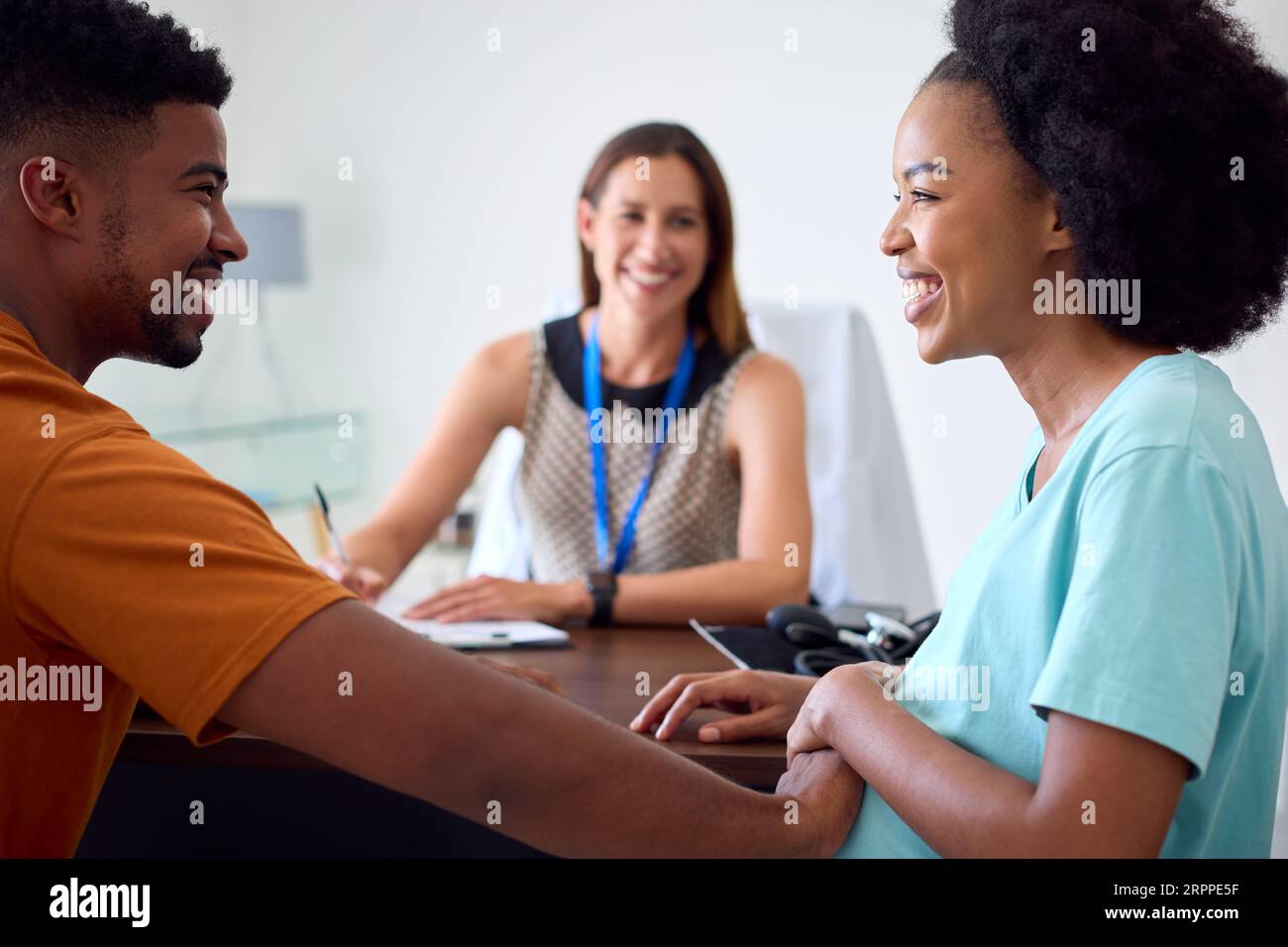 Pregnant Couple At Appointment With Female Doctor Or GP In Office Stock Photo