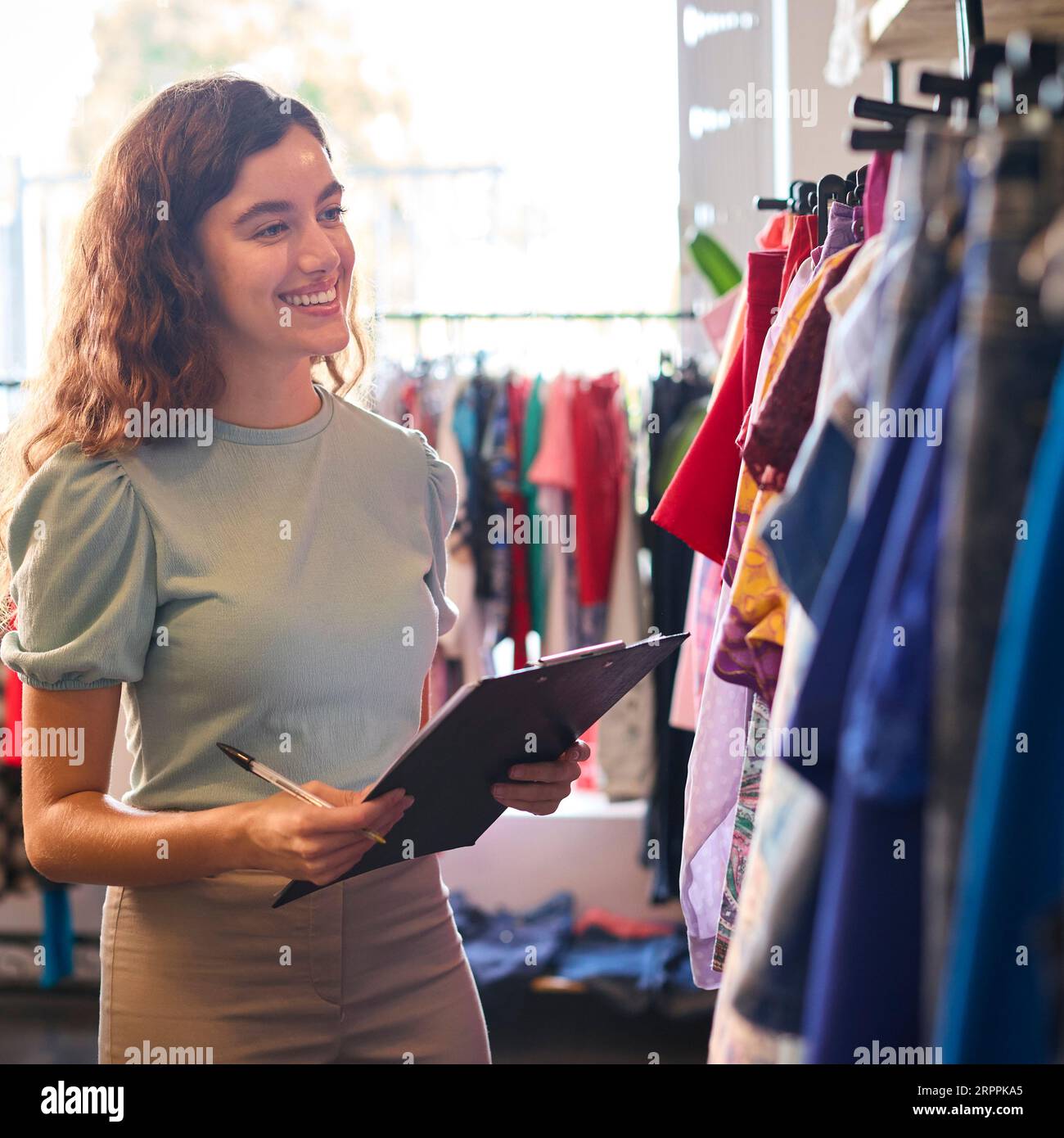 Female Owner Or Worker In Fashion Clothing Store Checking Stock With Clipboard Stock Photo