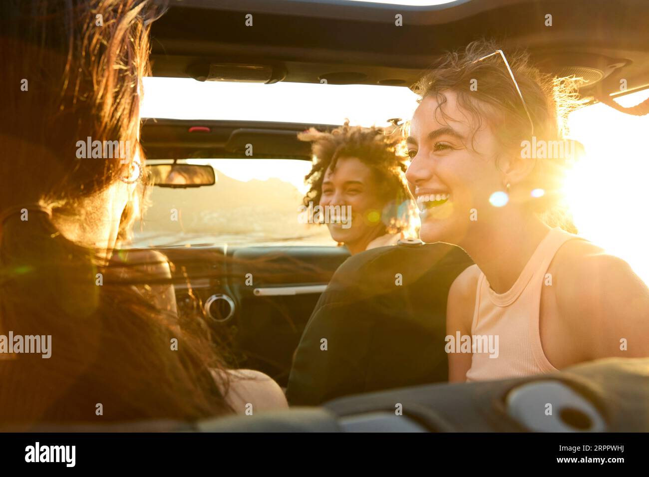 Group Of Laughing Female Friends Having Fun In Open Top Car On Road ...