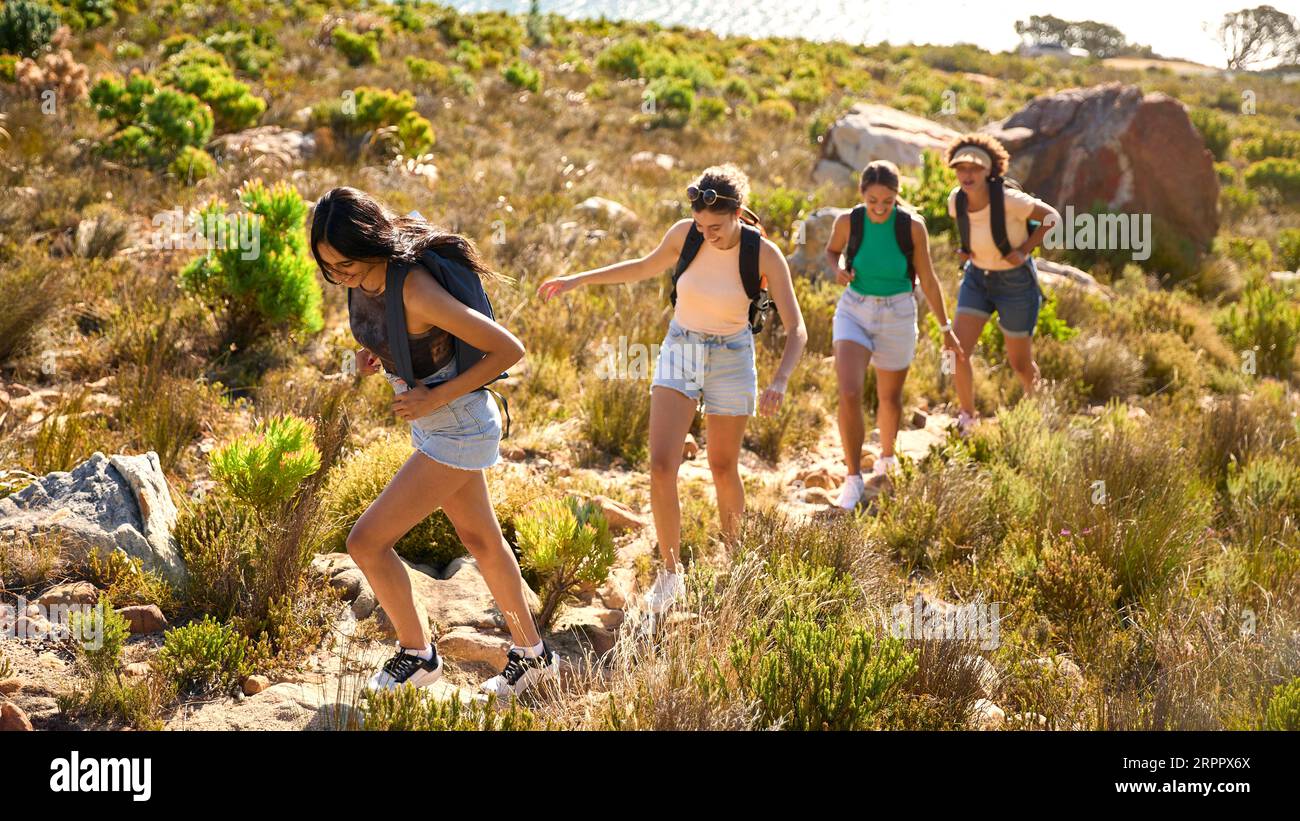 Group Of Female Friends With Backpacks On Vacation On Hike Through Countryside Next To Sea Stock Photo