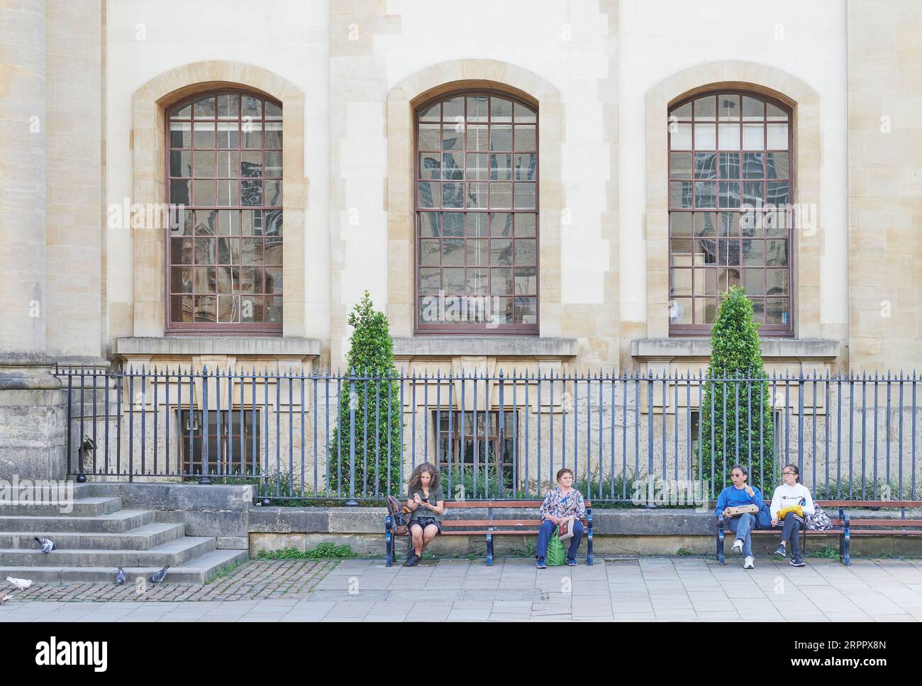 Tourists take a break on a bench outside the Weston Library, Bodleian Library, University of Oxford, England. Stock Photo