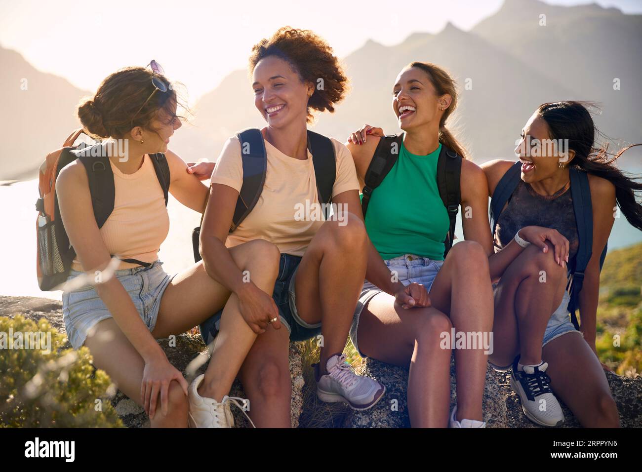 Female Friends With Backpacks On Vacation Taking A Break On Hike Through Countryside Stock Photo