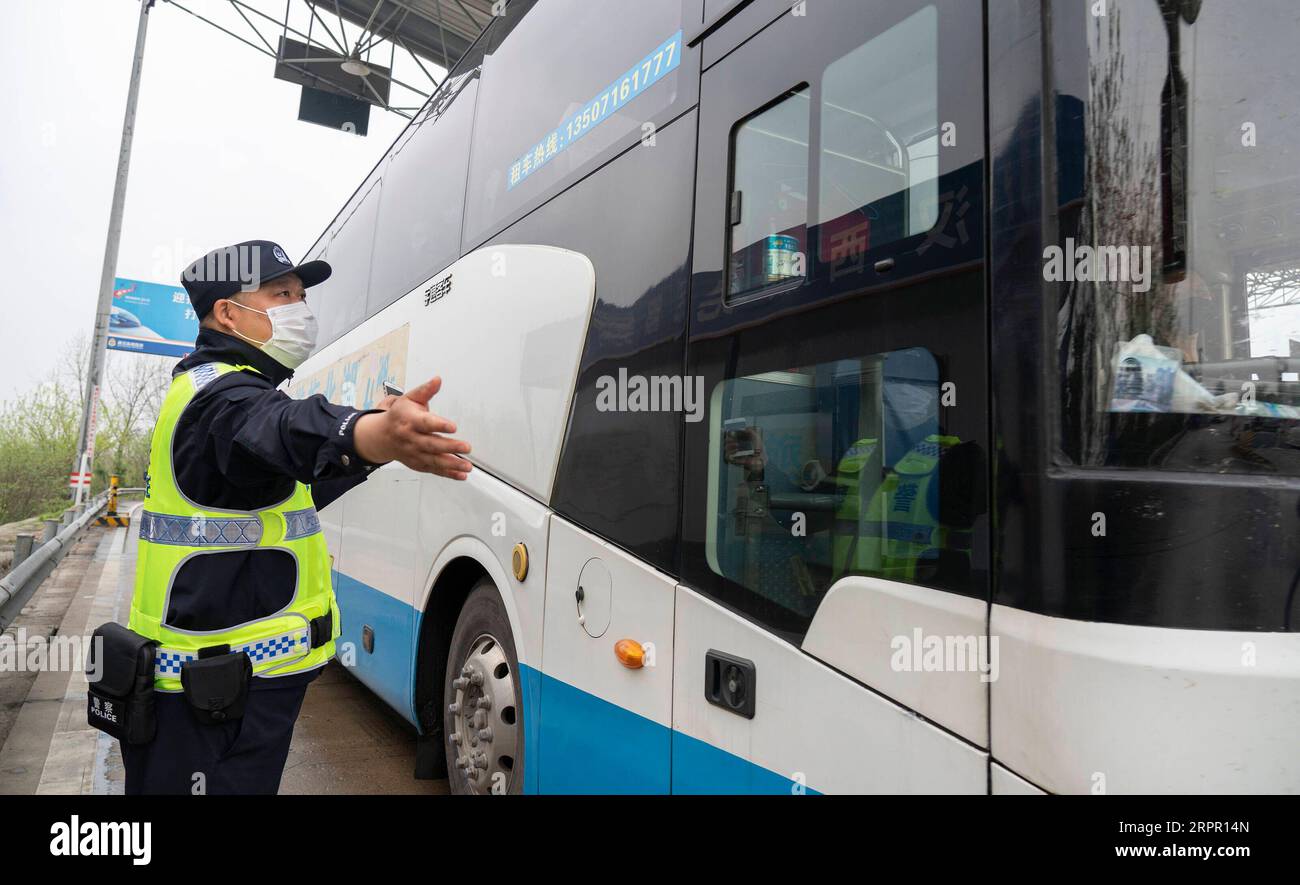 200324 -- WUHAN, March 24, 2020 -- Policeman Chen Gang gives a sign to permit a bus carrying returning workers to pass at a highway toll station in Wuhan, central China s Hubei Province, March 24, 2020. Wuhan, the Chinese city hardest hit by the novel coronavirus outbreak, will lift outbound travel restrictions from April 8 after over two months of lockdown, local authorities said Tuesday. People in Wuhan will be allowed to leave the city and Hubei Province, where Wuhan is the capital, if they hold a green health code, meaning no contact with any infected or suspected COVID-19 cases, according Stock Photo