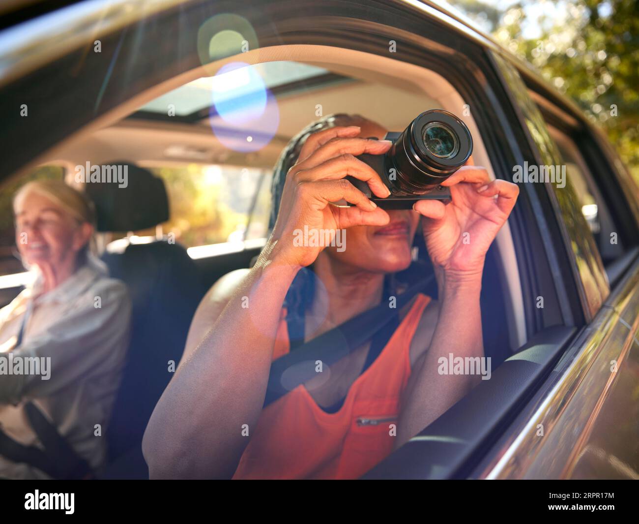 Passenger Taking Photo With Camera As Two Senior Female Friends Enjoy Day Trip Out In Car Stock Photo