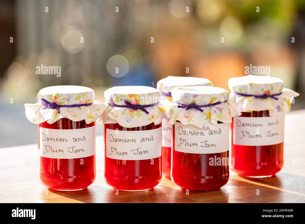 Jars of homemade Damson and plum jam. The glass jars have clear handwritten labels and each jar has a cloth topping. Stock Photo