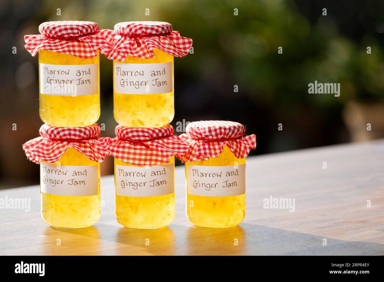 Jars of homemade Marrow and Ginger jam. The glass jars have clear handwritten labels and each jar has a gingham cloth topping. Stock Photo