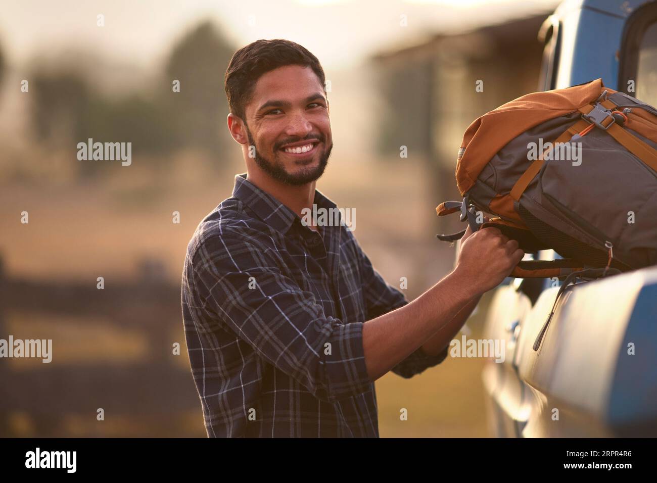 Portrait Of Man Loading Backpack Into Pick Up Truck For Road Trip To Cabin In Countryside Stock Photo