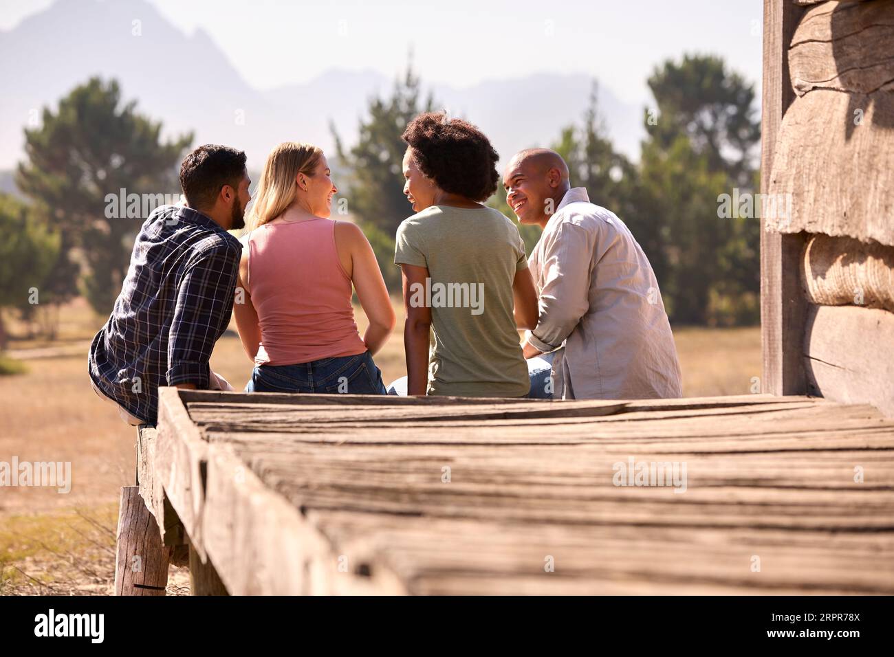 Rear View Of Group Of Friends On Vacation Sitting On Porch Of ...