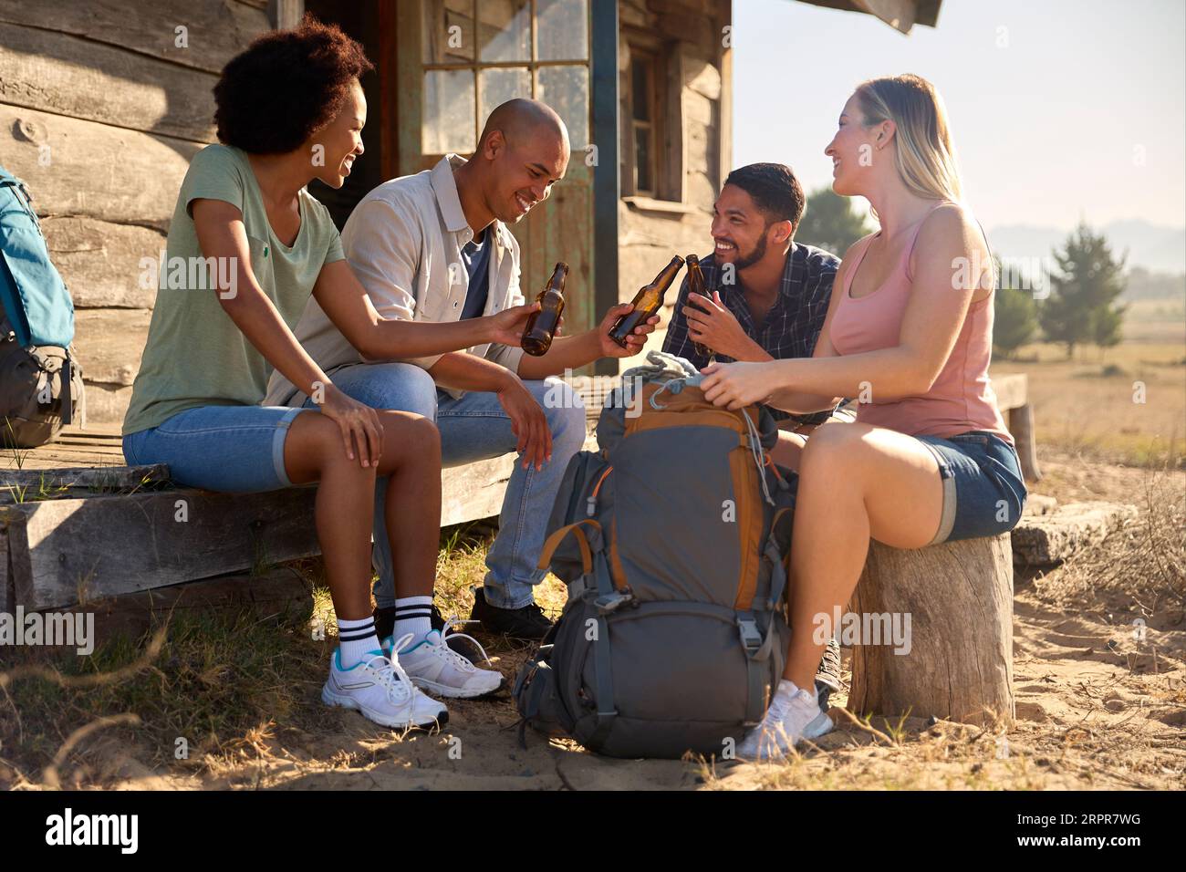 Group Of Friends On Vacation Sitting On Porch Of Countryside Cabin ...