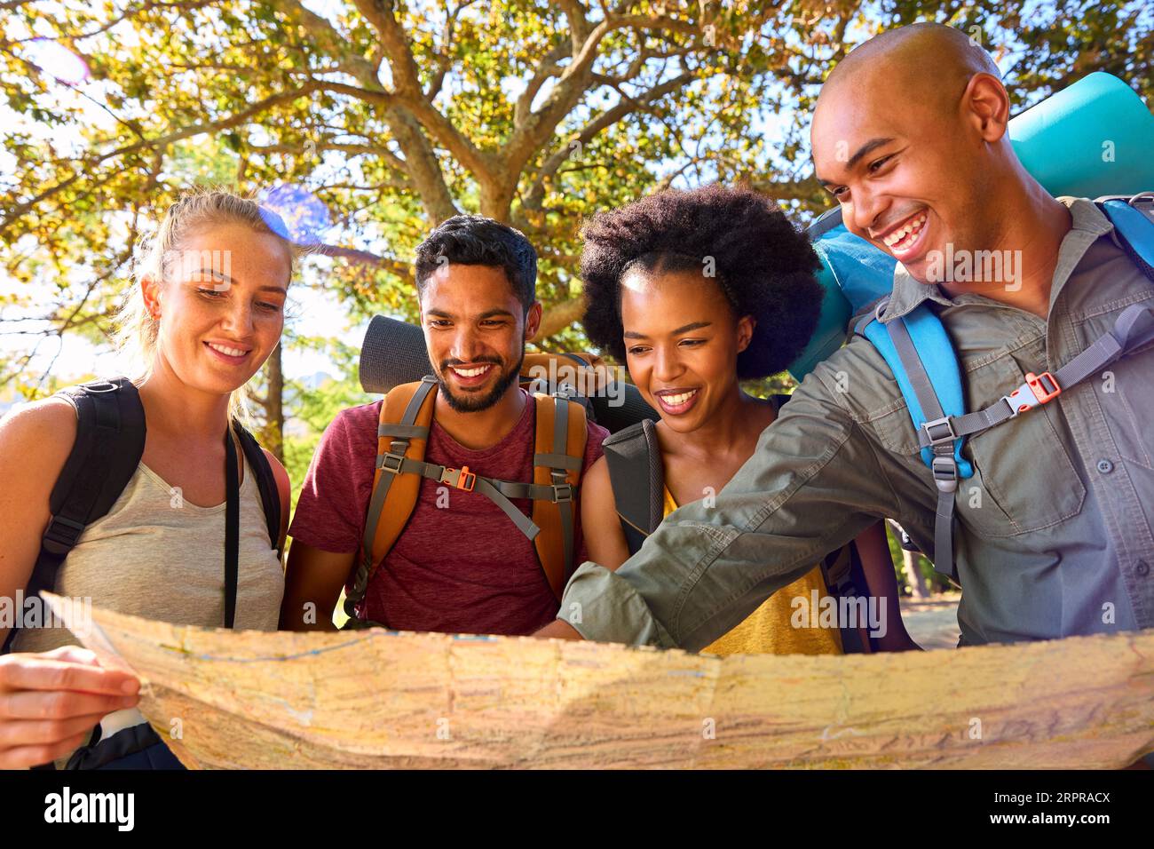 Group Of Friends With Backpacks Looking At Map On Vacation Hiking Through Forest Countryside Stock Photo