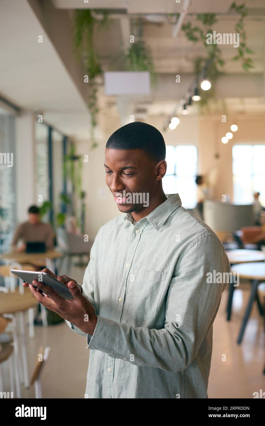 Businessman Standing In Busy Office Using Digital Tablet Stock Photo