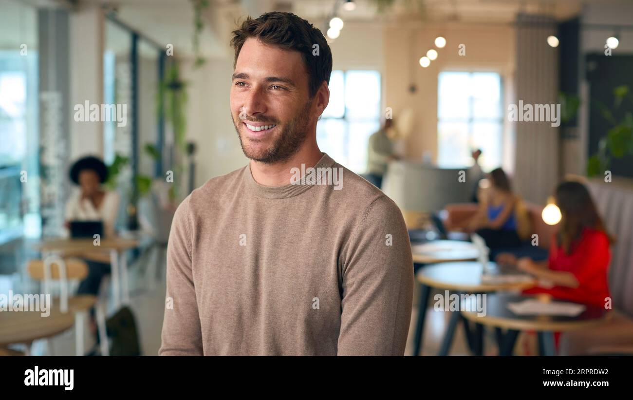 Portrait Of Smiling Businessman Standing In Busy Office Stock Photo