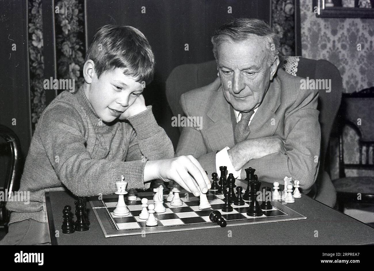 1980, sitting with his grandfather inside a front rom a young boy playing a game of chess with him, England, UK. Chess is a popular board game of strategic skill involving two players, with the object to make escape of the opponent's king impossible. Stock Photo