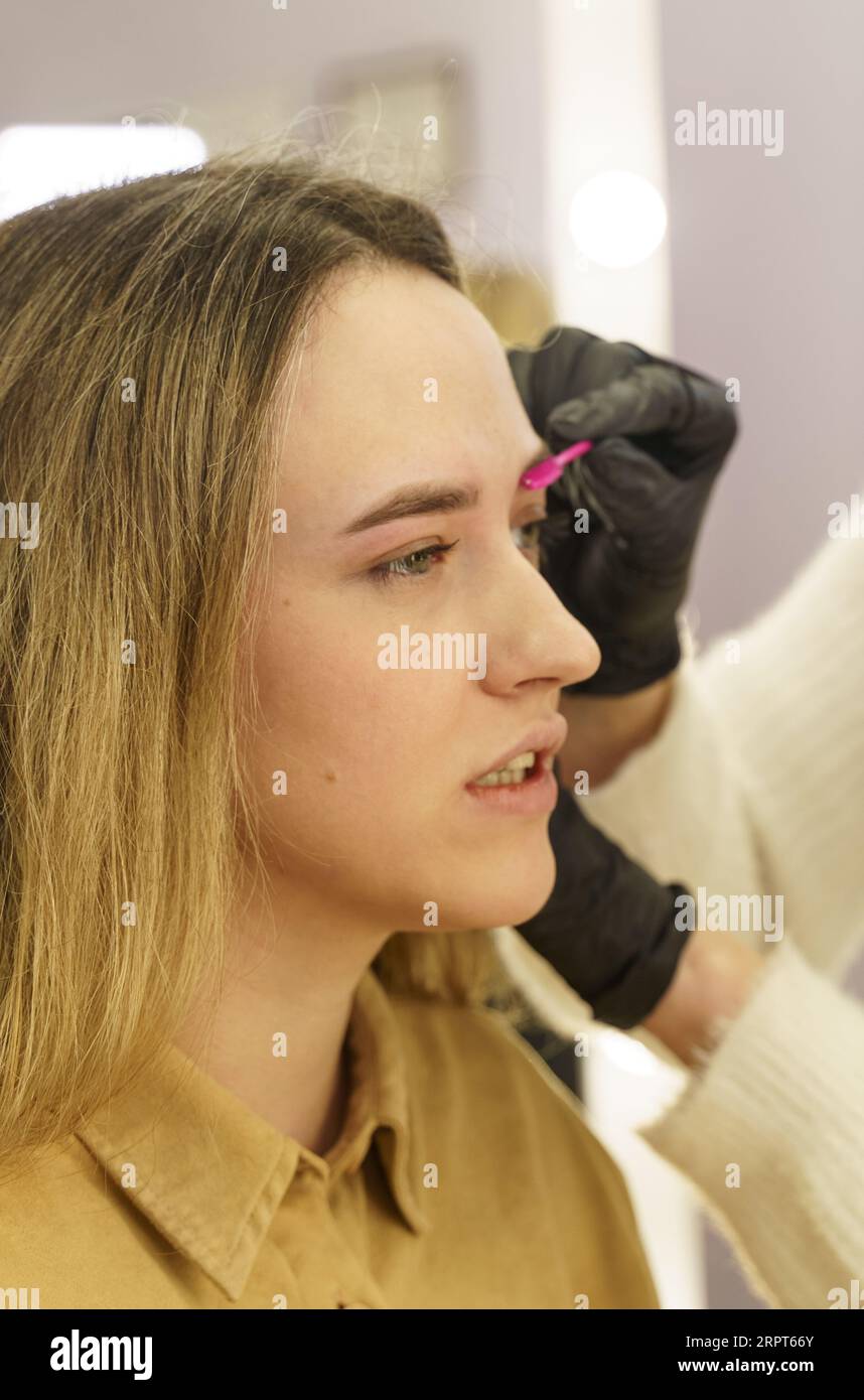 Portrait of a woman having her eyebrows plucked with tweezers in a beauty salon. After the procedure, the client is satisfied with the services, sends Stock Photo