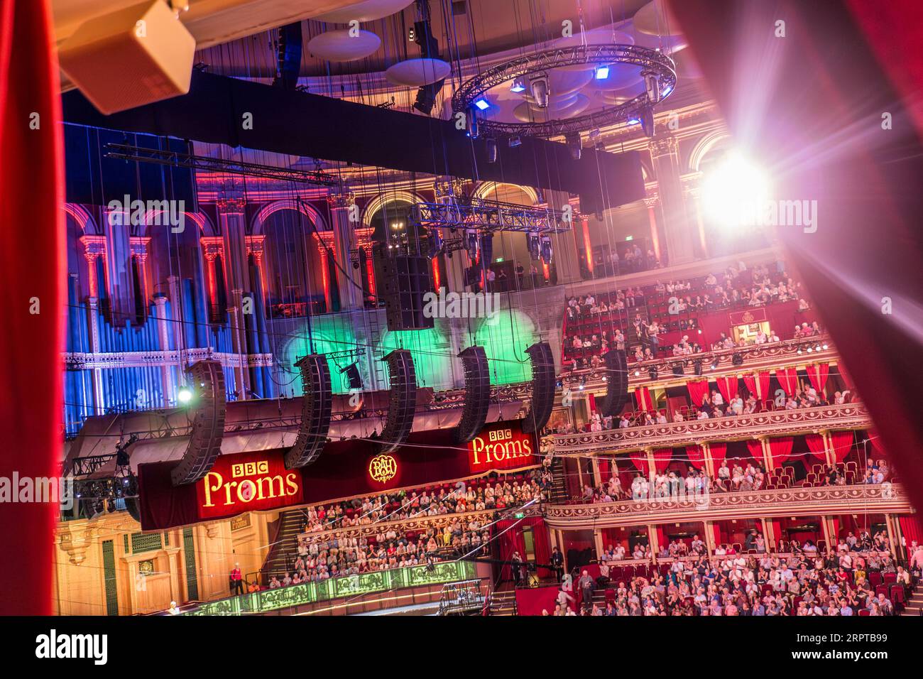 ALBERT HALL PROMS CONCERT PERFORMANCE  INTERIOR OPENING UNVEILING SHOWTIME WITH BBC PROMS SIGNS viewed through red velvet curtains of private box with television lights flaring to the auditorium, audience and stage. Royal Albert Hall, Kensington Gore, Kensington, London, United Kingdom Stock Photo