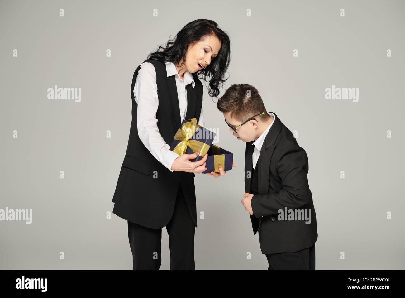 woman in formal wear presenting gift to surprised son with down ...