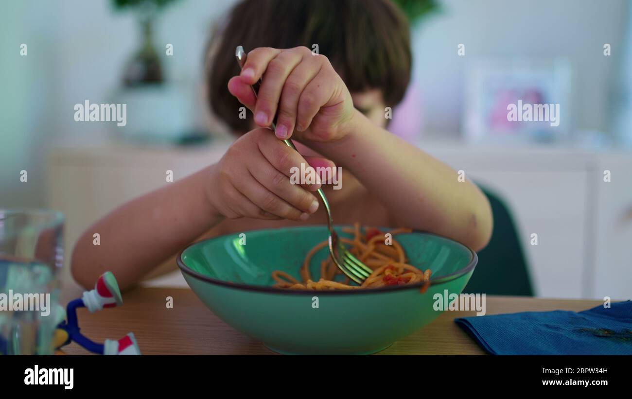 Closeup small boy eating pasta noodles, twisting and turning spaghetti
