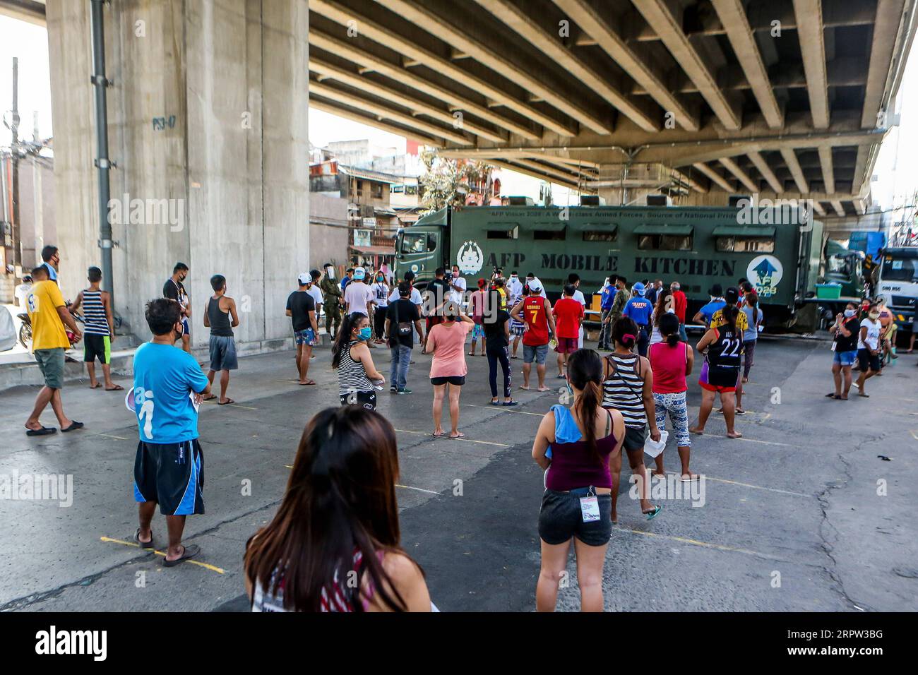 Residents wearing face masks hold their plates and bowls as they line ...
