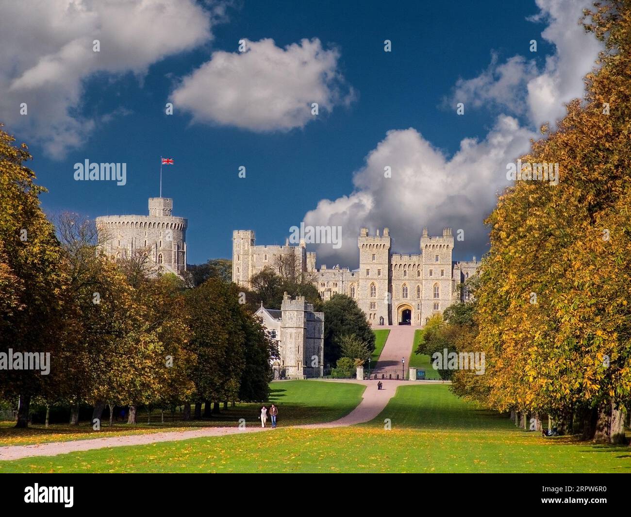 Windsor Castle flying the Union Jack Flag viewed down the Long Walk illuminated by dramatic sunlight between clouds. landscape Windsor Berkshire  UK Stock Photo